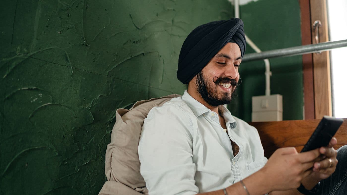 An Indian man smiling while texting on his phone